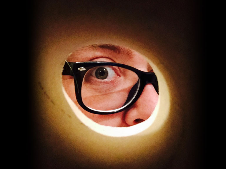 A person with glasses is looking through a cardboard tube